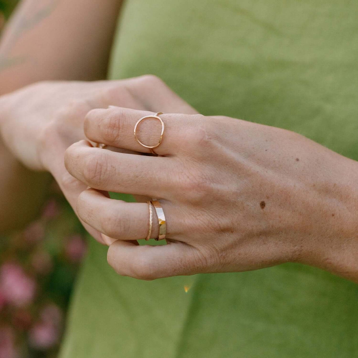 Close-up of a hand wearing two gold rings with a blurred green background