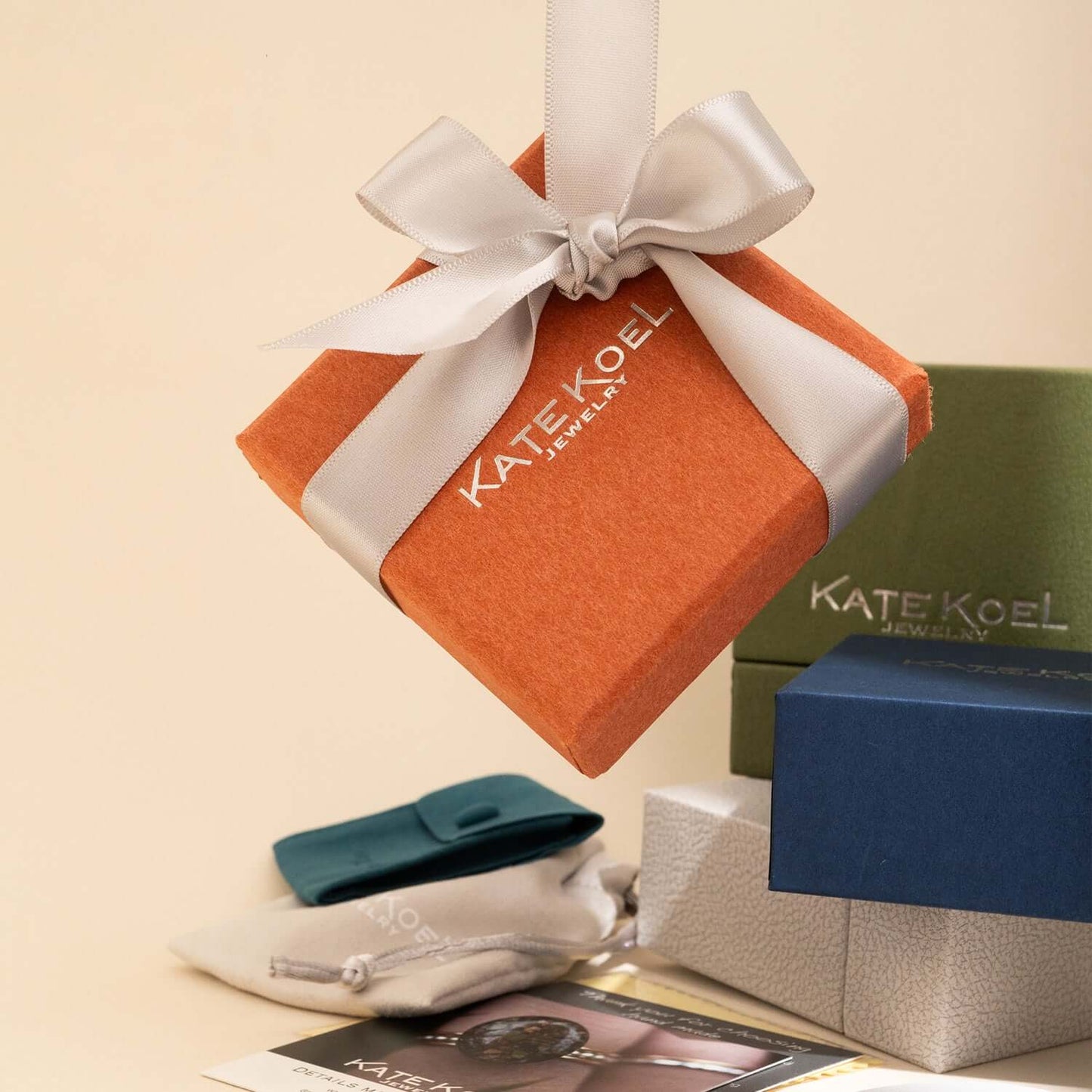 Orange jewelry box with a white ribbon, green and blue boxes, and accessories on a beige background.