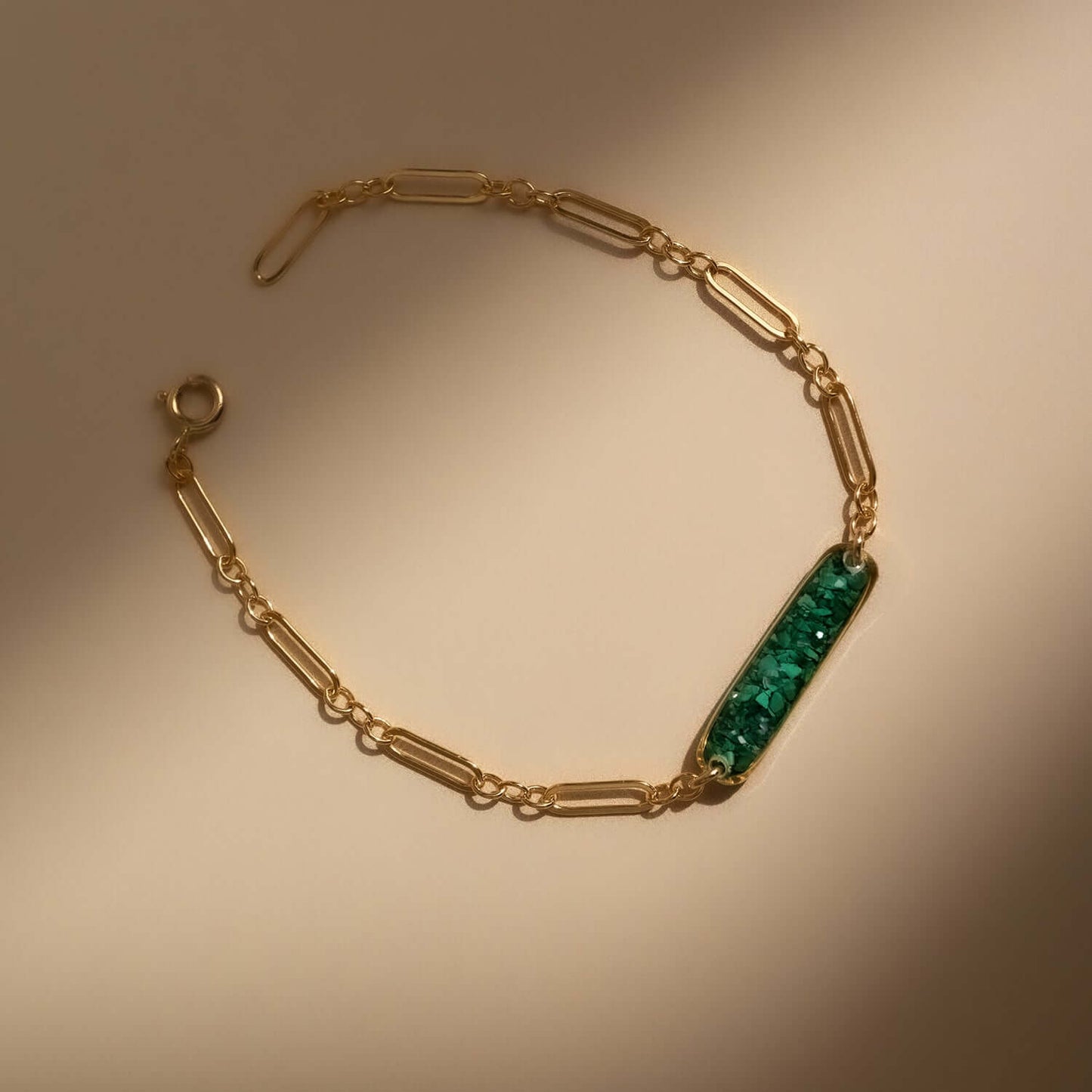 A green malachite bar bracelet with a green and gold geometric patterned pendant on a 14K gold filled chain, displayed on a light background.