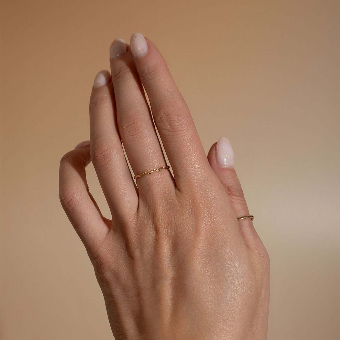 Hand wearing a gold ring on a beige background