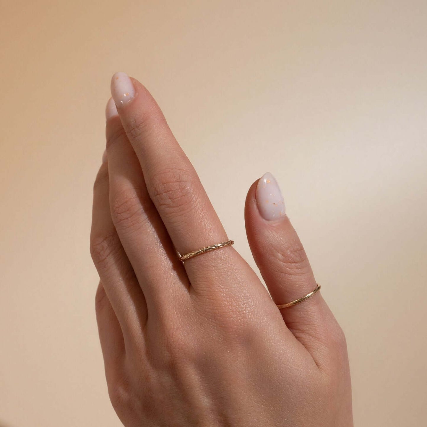 Hand wearing two gold rings on a beige background
