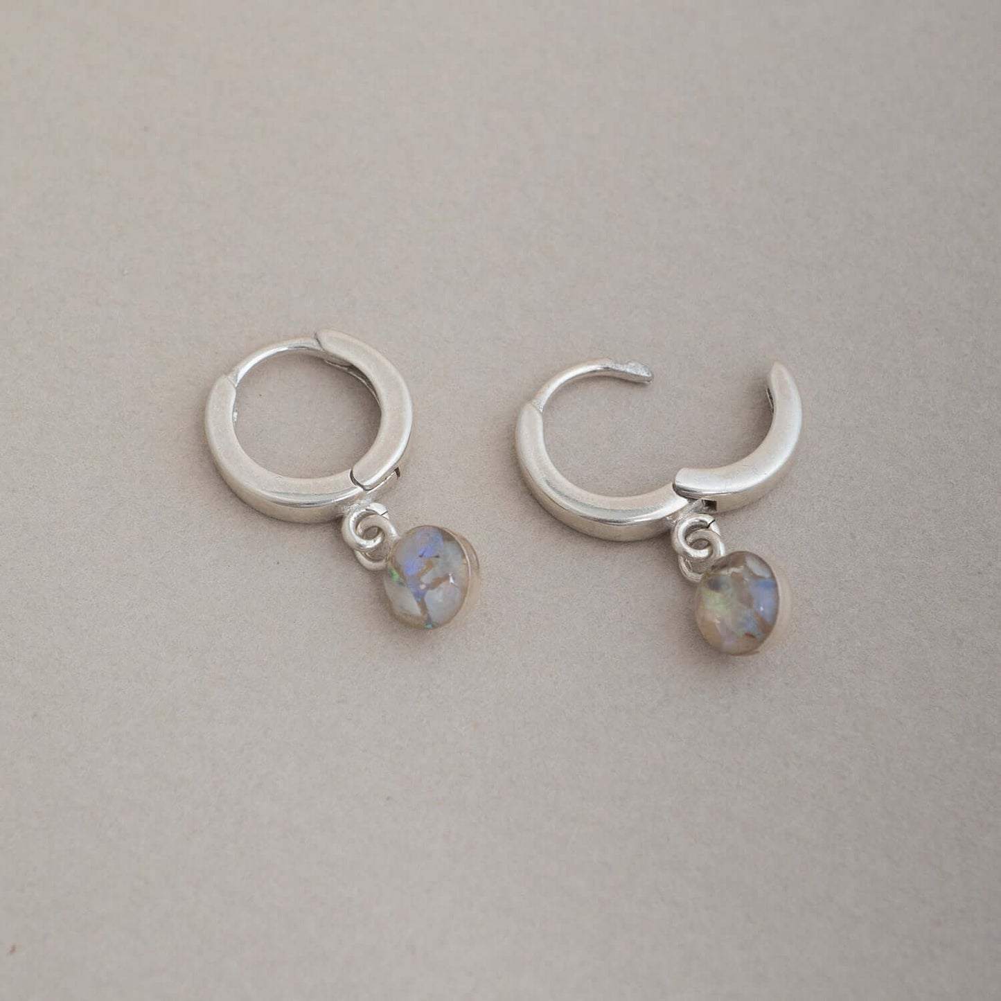 Pair of silver hoop earrings with moon-shaped charms and small stones on a light gray background