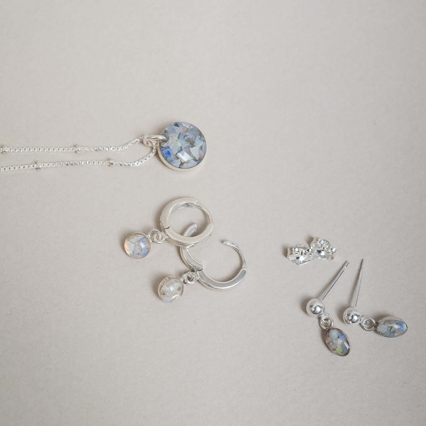 Silver jewelry set including necklace, hoop earrings, and stud earrings on a light gray background