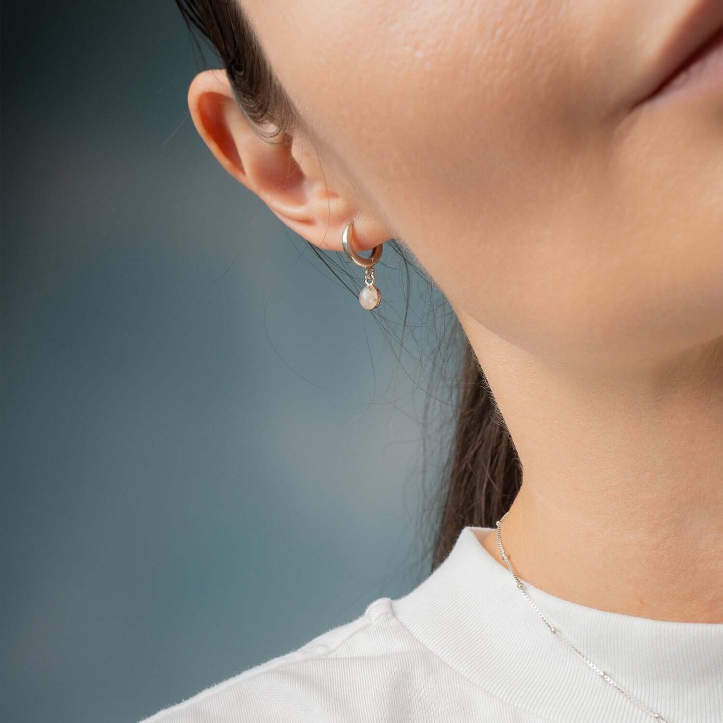 Close-up of a person wearing a pearl earring against a blurred background
