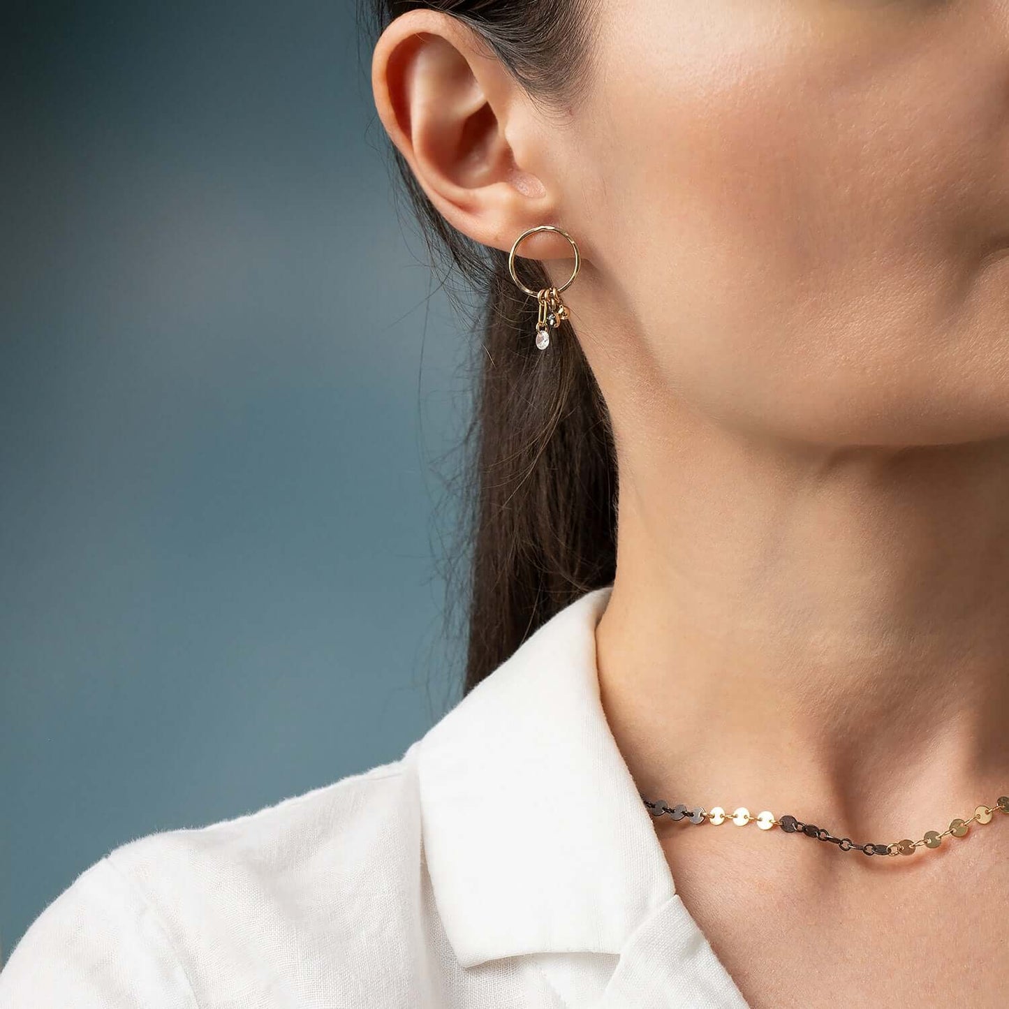 Close-up of a person wearing gold hoop earrings with pink gemstones against a neutral background
