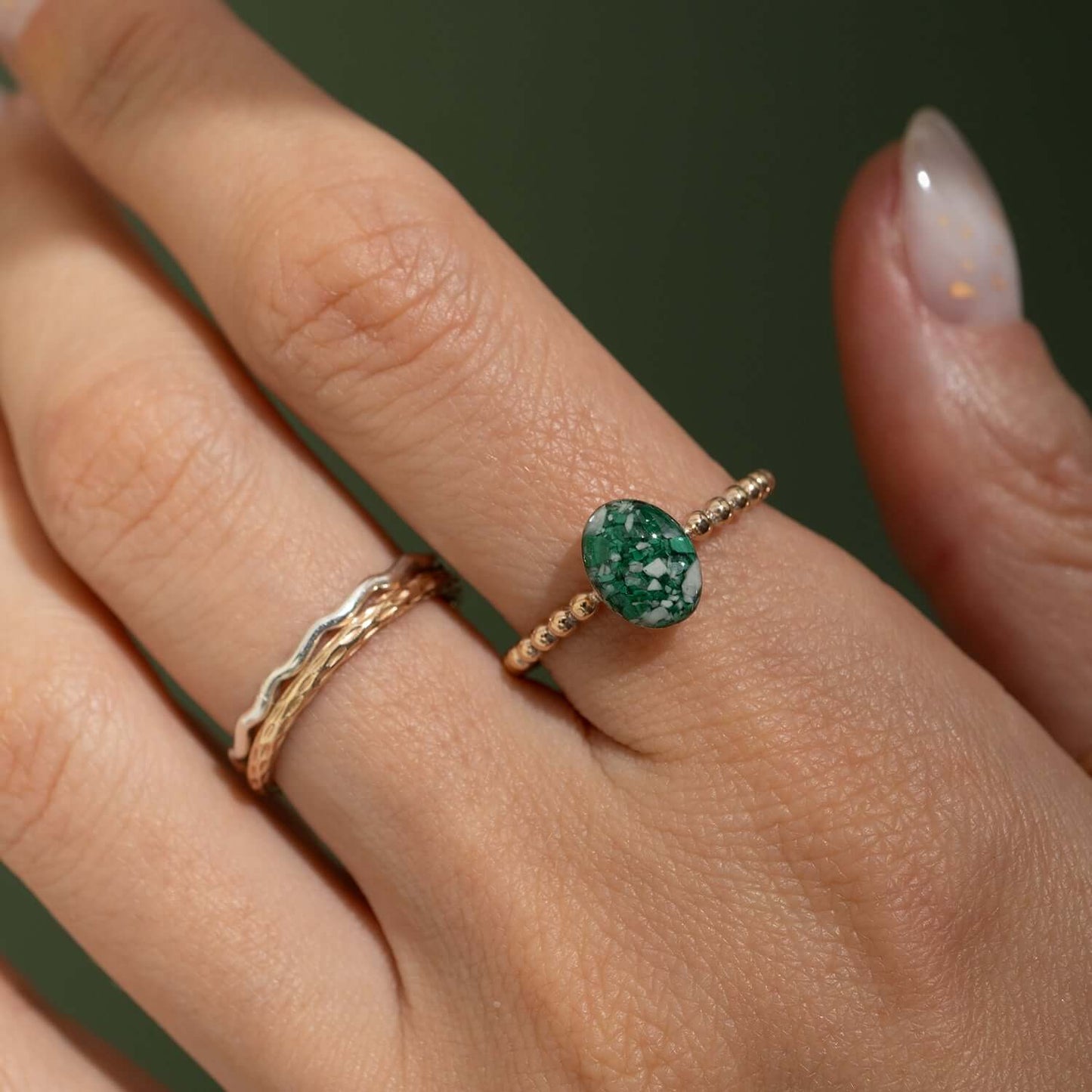 Close-up of a hand wearing two gold rings with green gemstones on a dark background