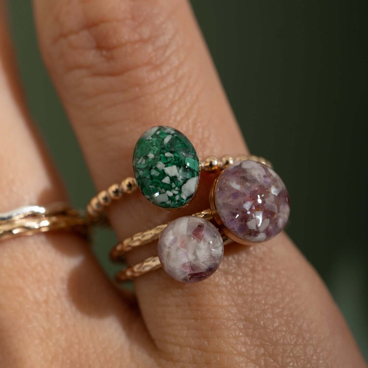 Close-up of a hand wearing three gold rings with gemstones on a blurred background