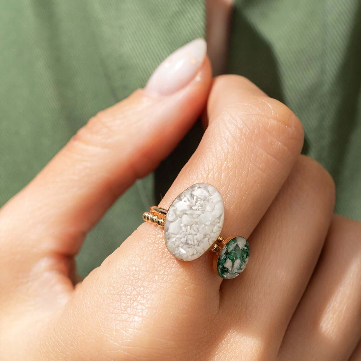 Close-up of a hand wearing a ring with two stones on a green fabric background