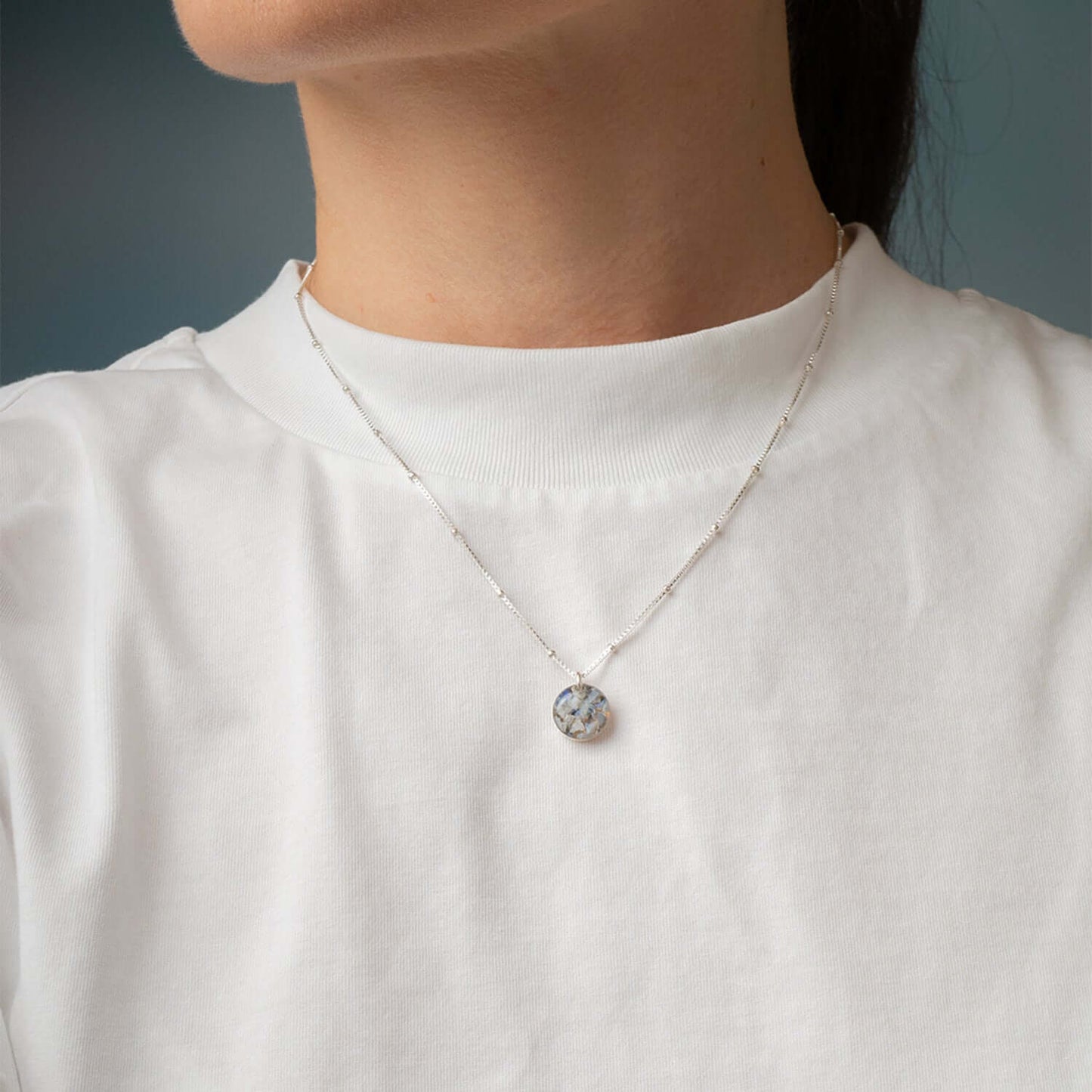 Person wearing a silver necklace with a pendant against a neutral background