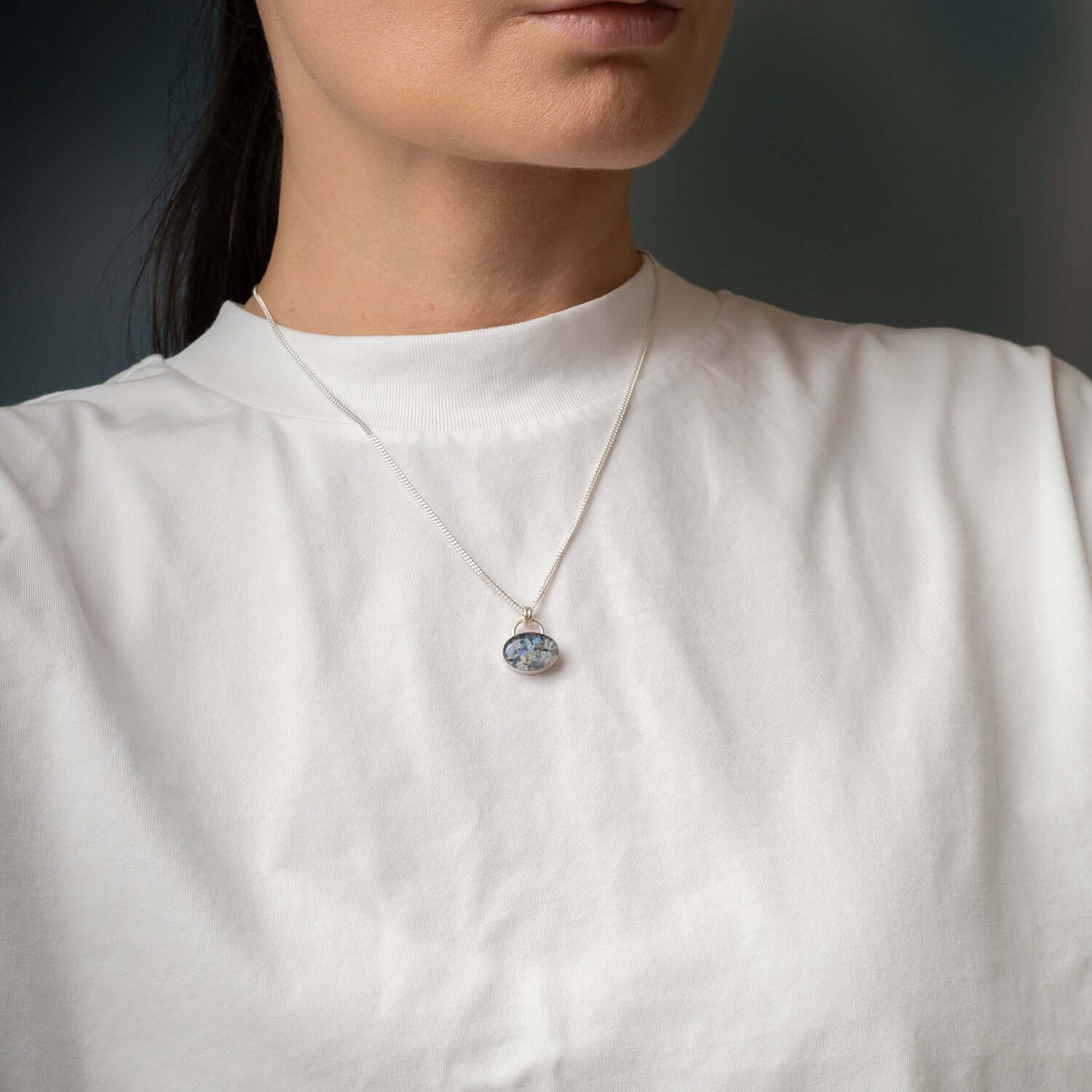 Person wearing a necklace with a pendant against a neutral background