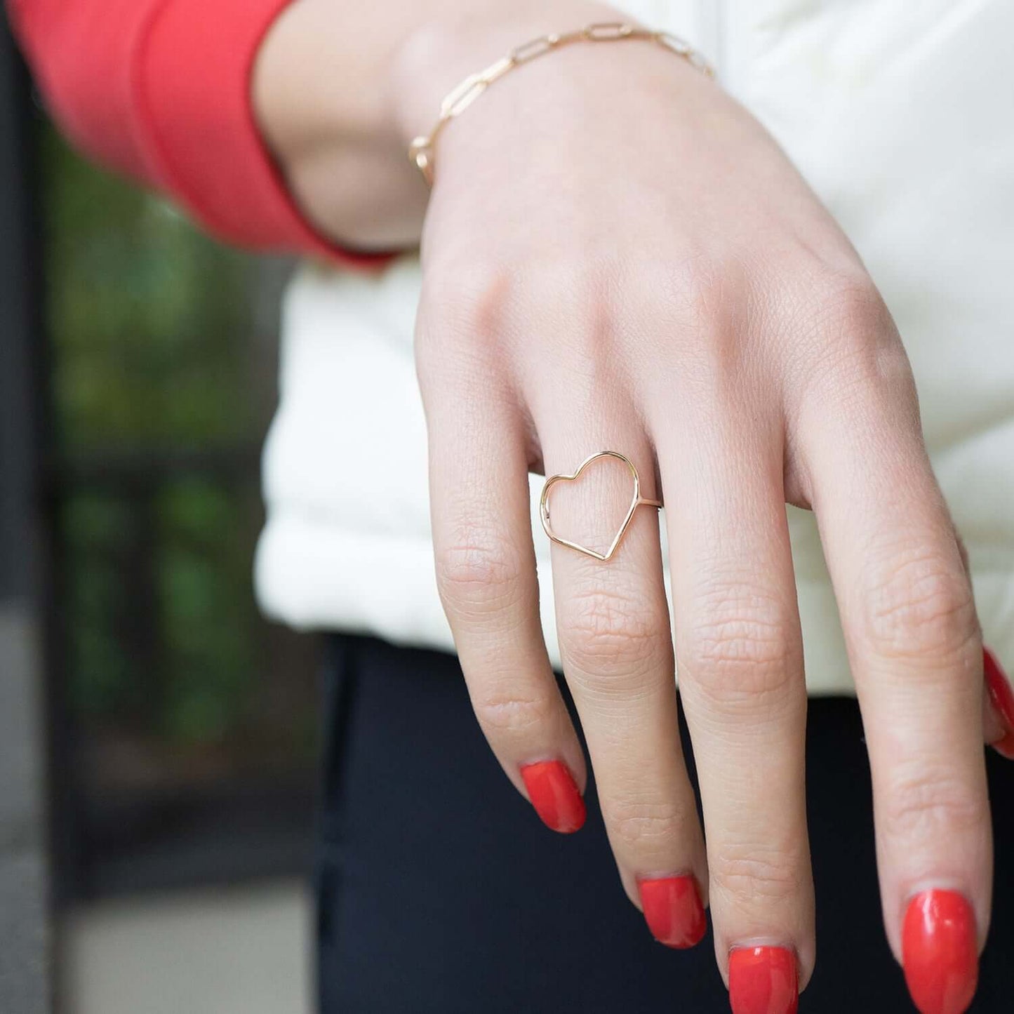 Hand wearing a heart-shaped ring with red nail polish against a blurred background