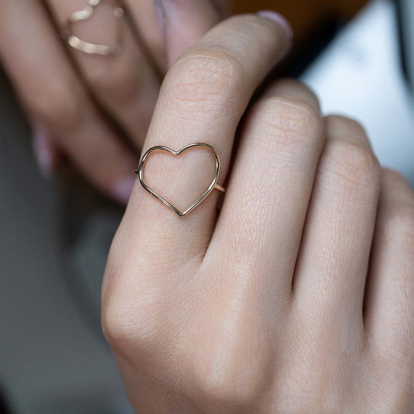 Gold heart-shaped ring on a finger with a blurred background