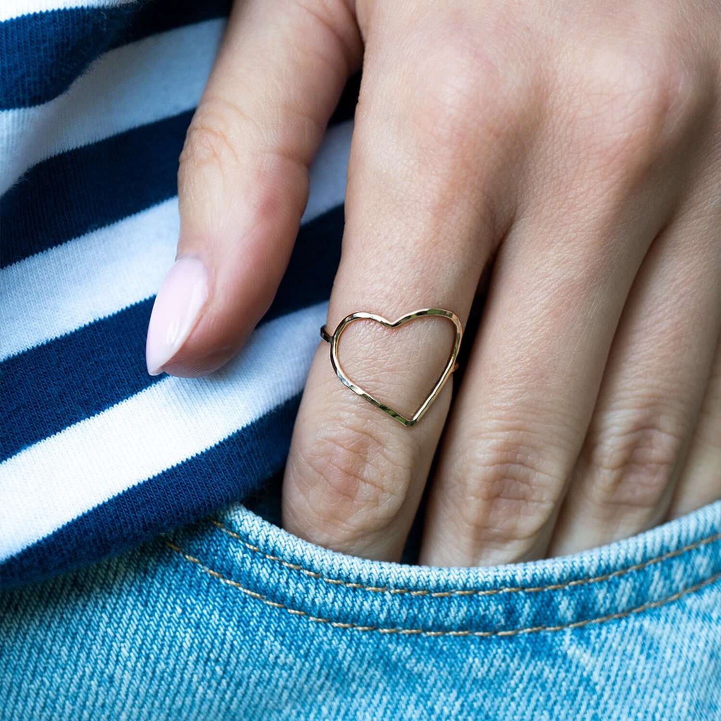 Hand wearing a gold heart-shaped ring with a blue and white striped fabric background