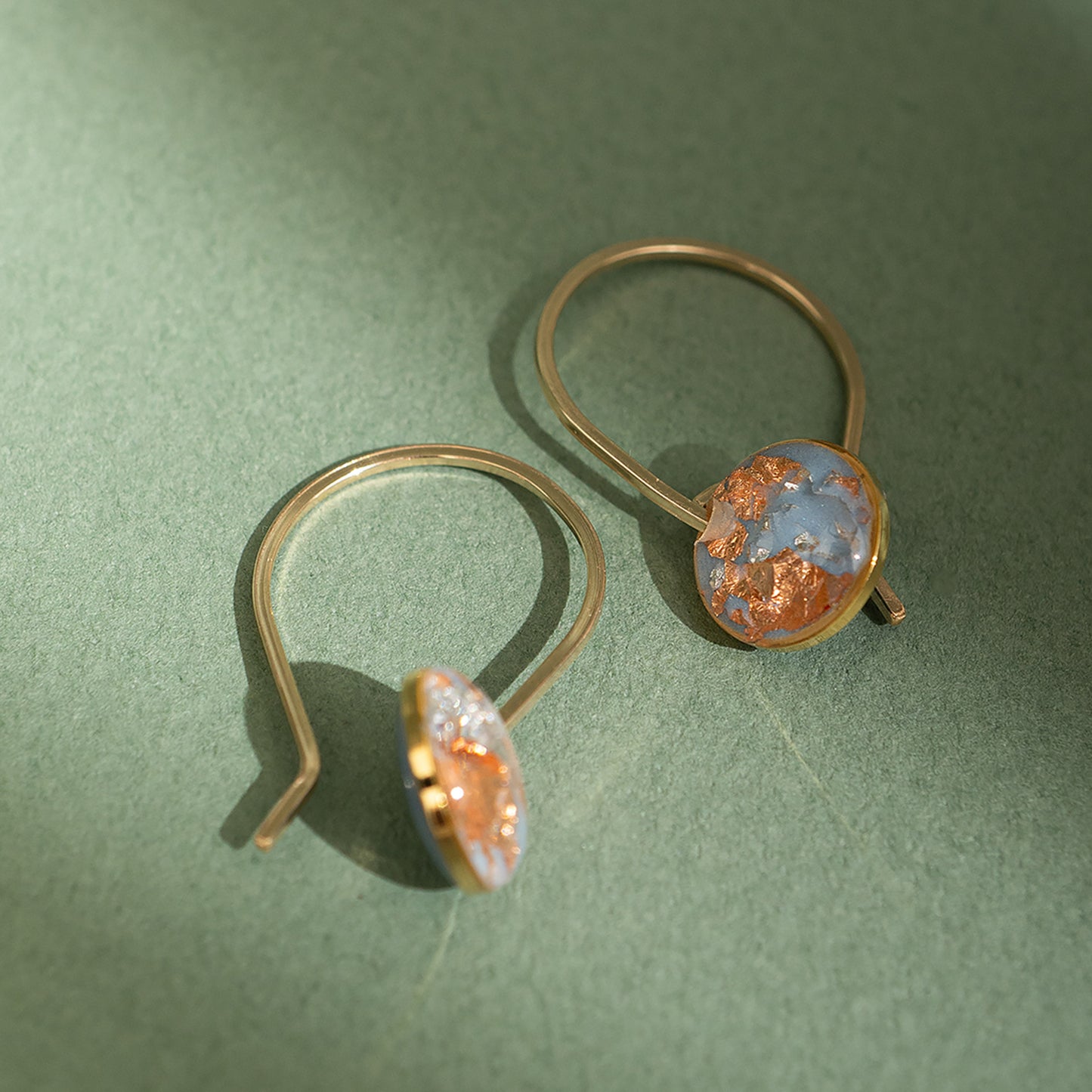 Close-up of a person wearing gold hoop earrings with a sky blue gemstone with silver and copper foils inside