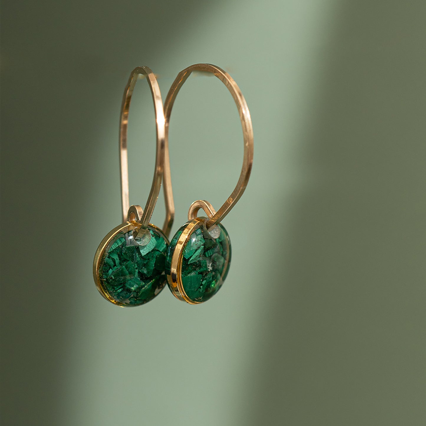 A pair of gold-filled round hoop earrings with a crystal infused with crushed gemstones, displayed against a green background.