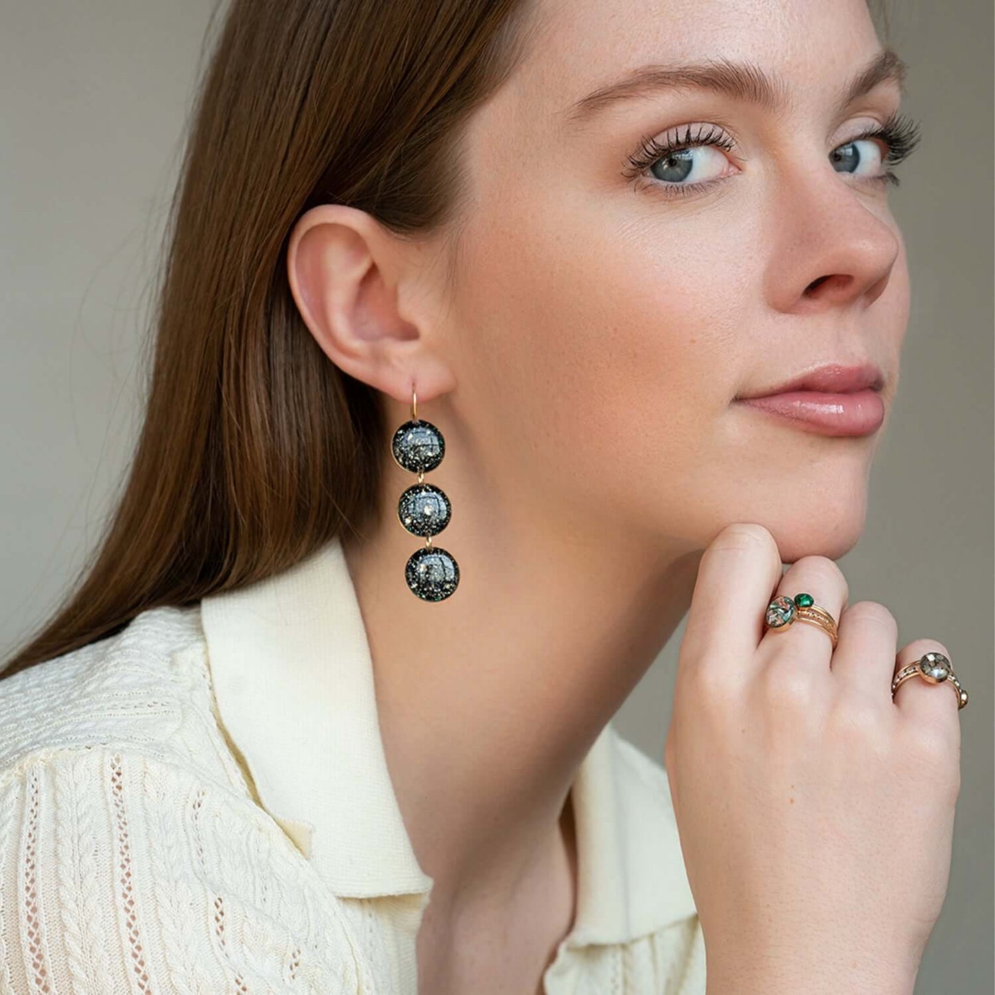 Woman wearing a set of earrings and rings with a neutral background