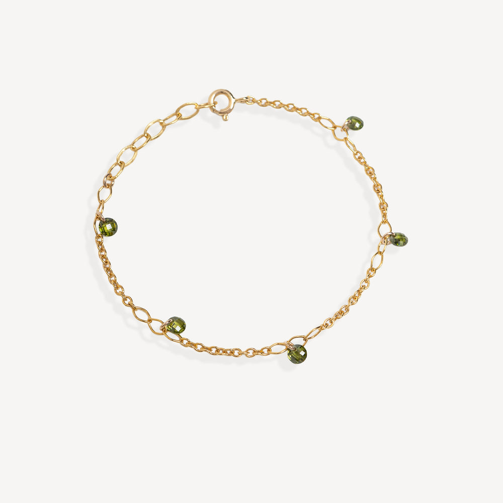 A delicate gold chain bracelet with small green faceted bead charms, displayed on a clean off-white background.