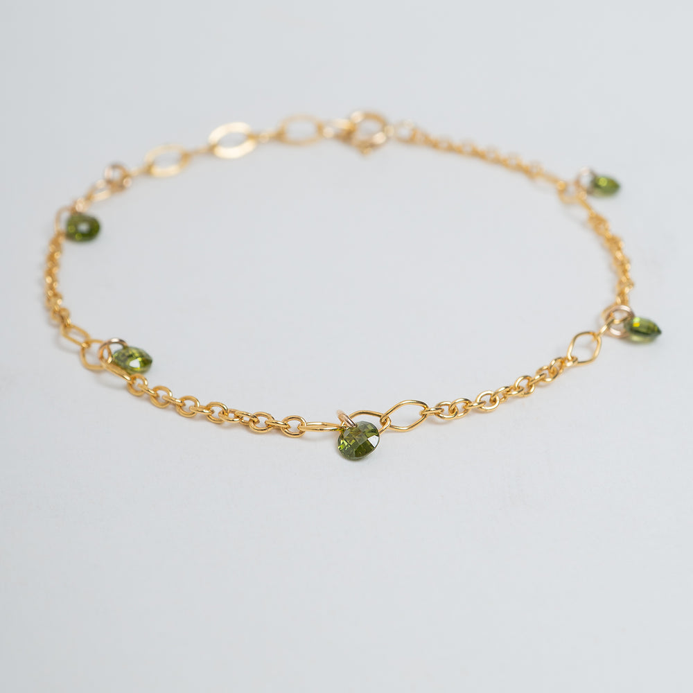 A delicate gold chain bracelet with small green faceted bead charms, displayed on a clean off-white background.