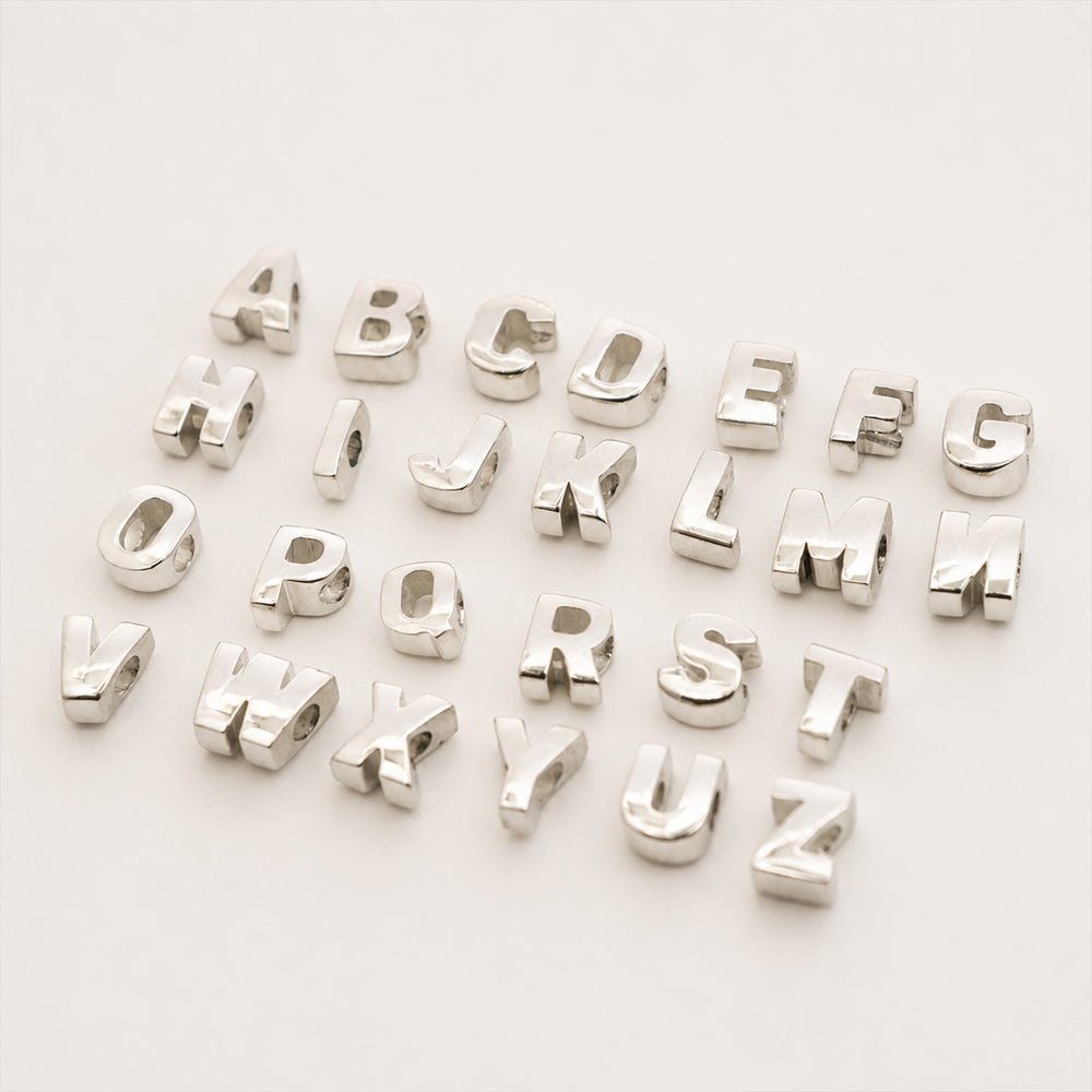 Two gold-tone chain necklaces laid on a light neutral background, each paired with a row of silver-tone initial charms spelling out names.