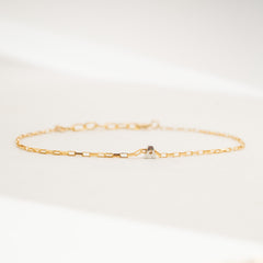 A delicate gold chain bracelet with a small central silver-toned geometric charm, displayed on a clean white surface.