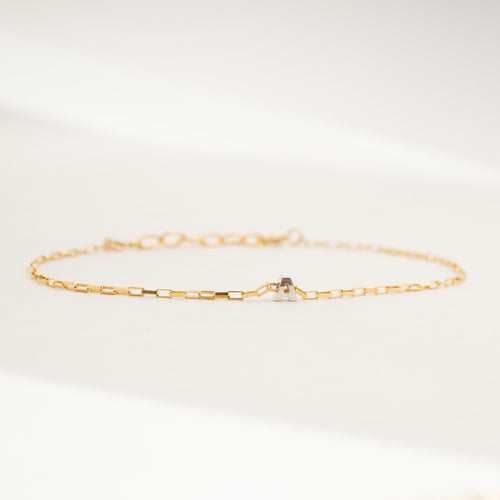A delicate gold chain bracelet with a small central silver-toned geometric charm, displayed on a clean white surface.