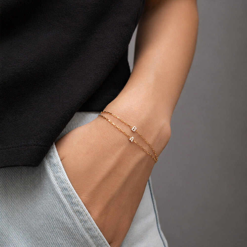 Two gold-tone chain necklaces laid on a light neutral background, each paired with a row of silver-tone initial charms spelling out names.