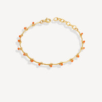 Gold bracelet with small orange beads on a white background