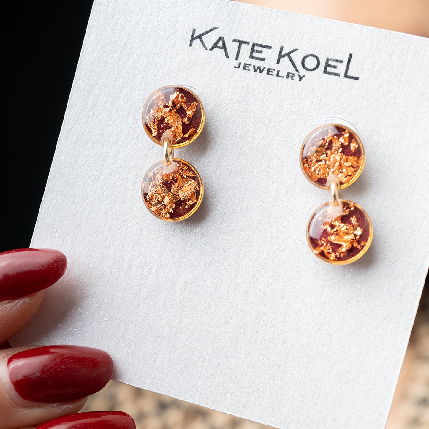 Gold and amber earrings on a Kate Koel Jewelry card with red nail polish.