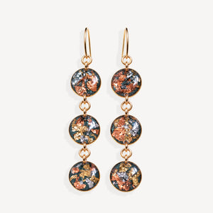 A pair of gold-tone dangle earrings with three circular glass disc charms each featuring a colorful metallic foil pattern of copper, gold, and silver on a dark background, set against a plain off-white background.