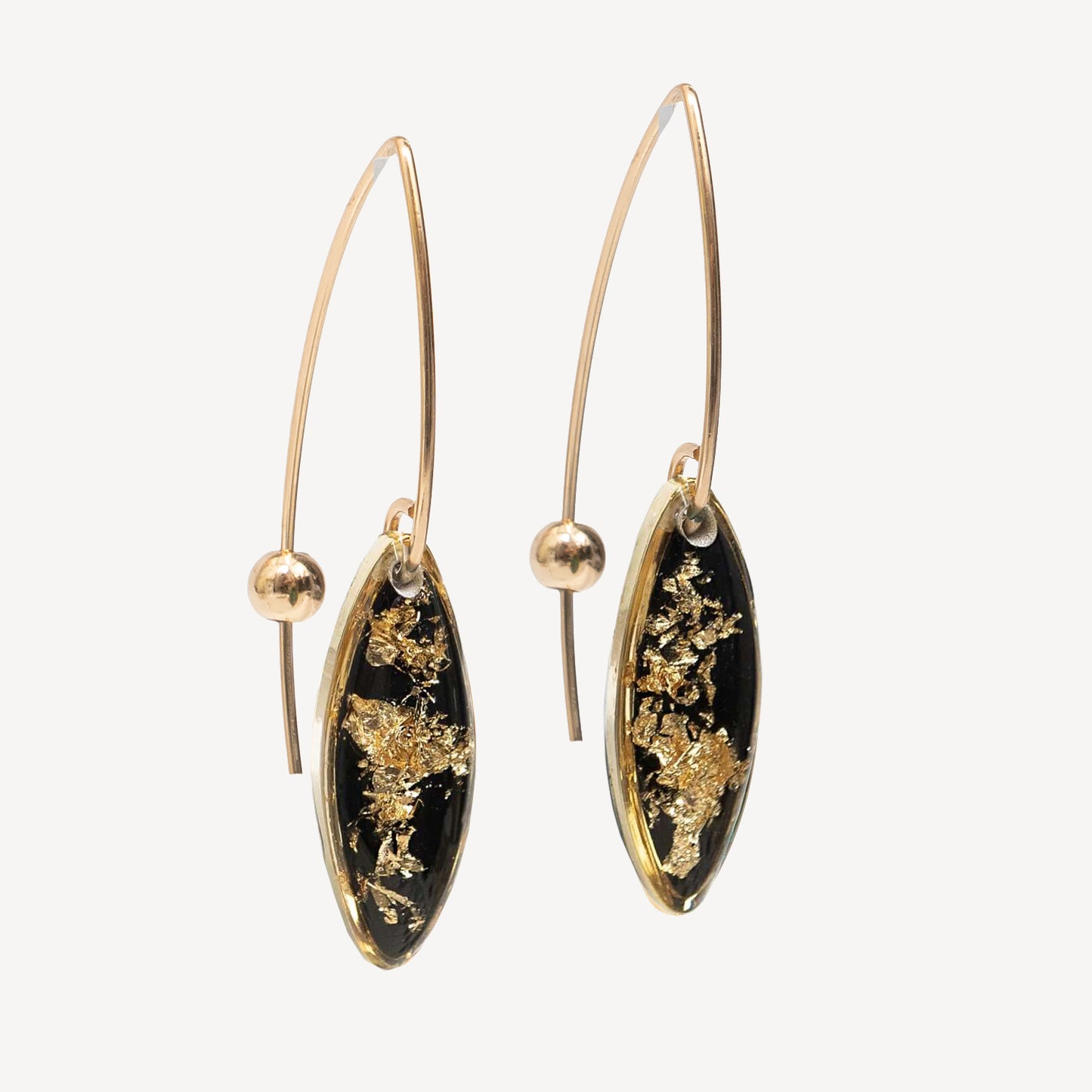 A pair of gold hoop earrings with marquise-shaped black dangles featuring embedded gold leaf, shown against a light gray background.