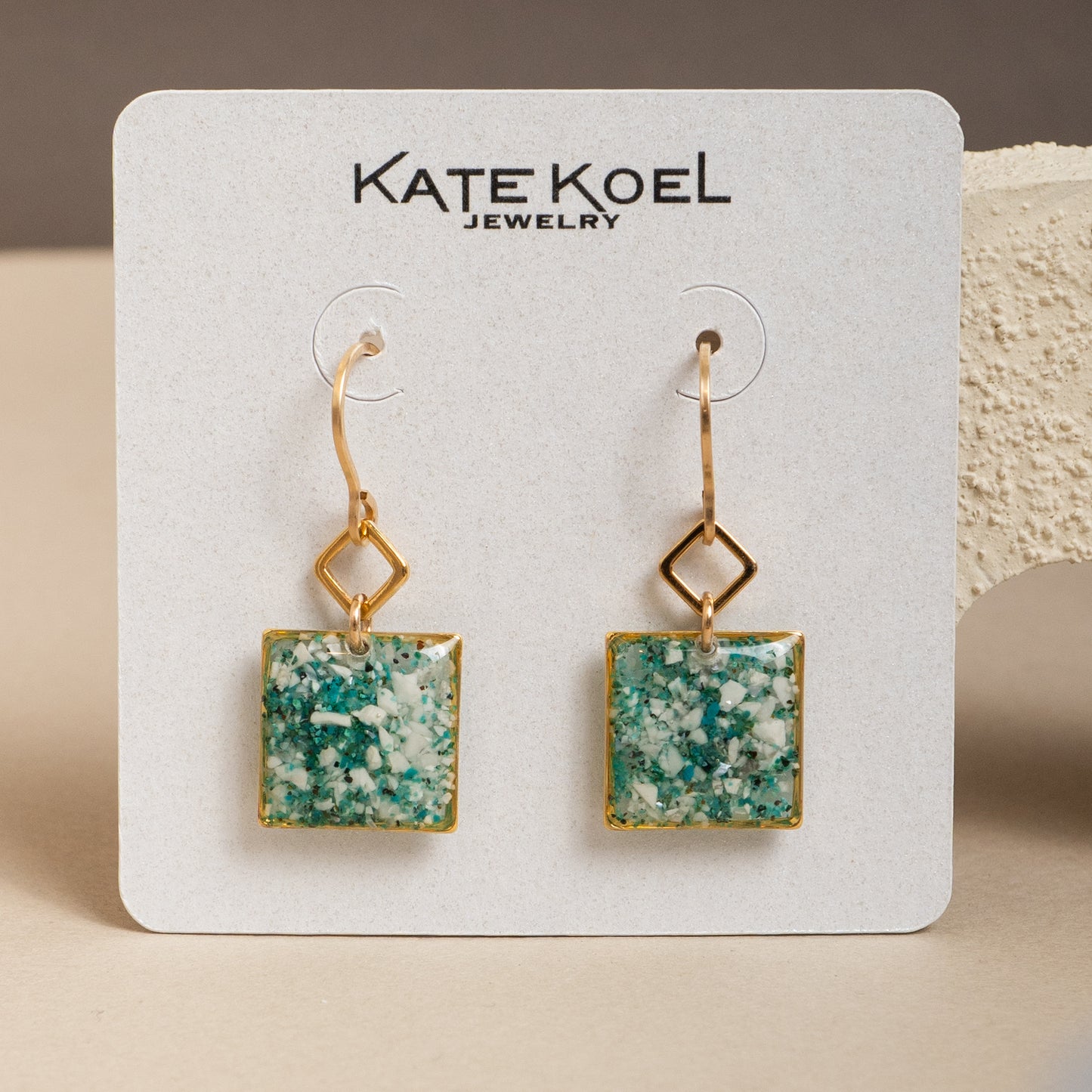 Square green earrings with gold frames on a Kate Koel Jewelry card.