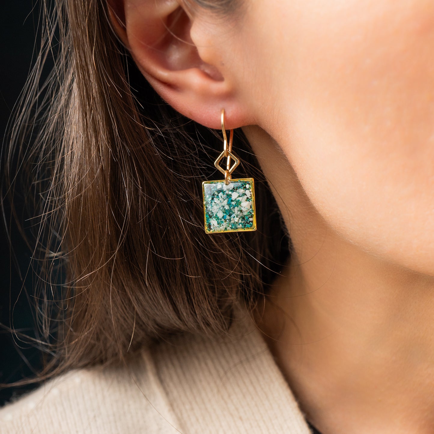 Close-up of a person wearing a gold earring with a green square pendant.