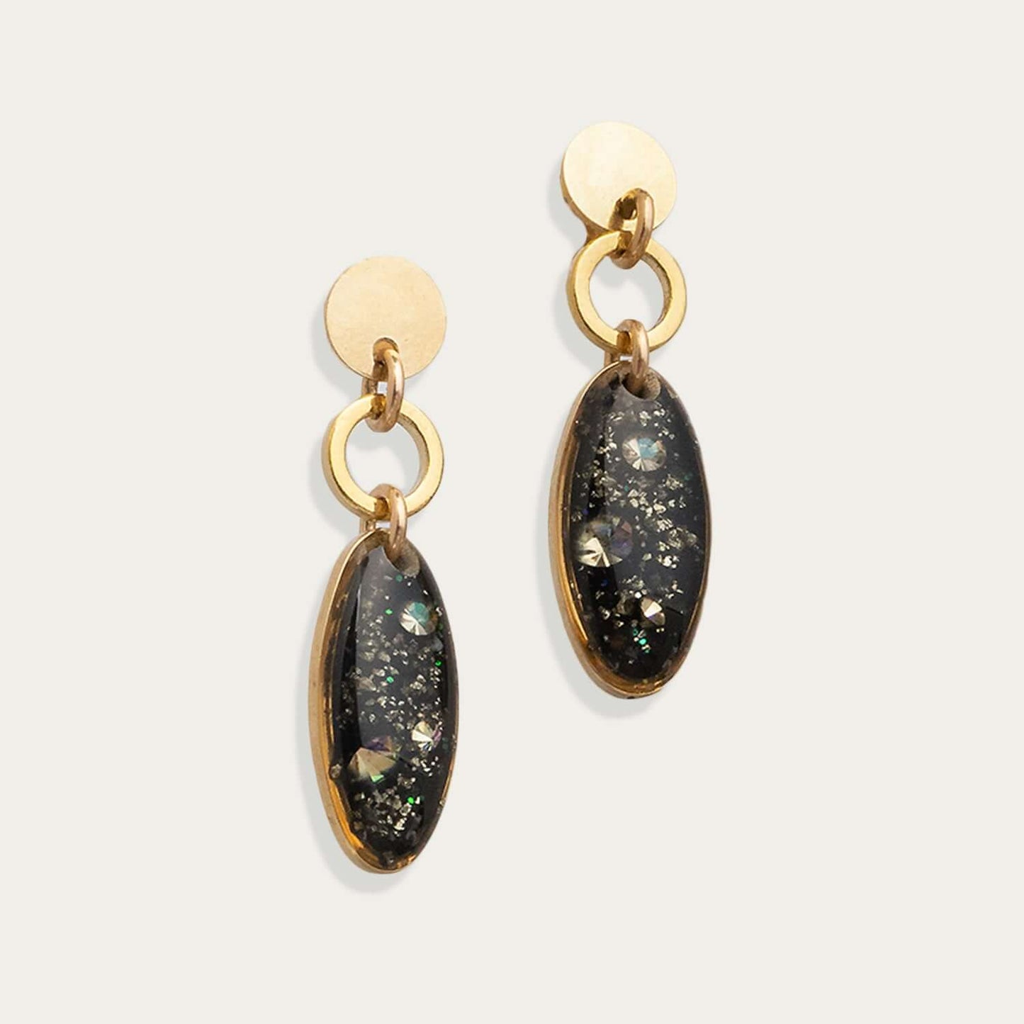 Gold earrings with dark gemstones on a light gray background