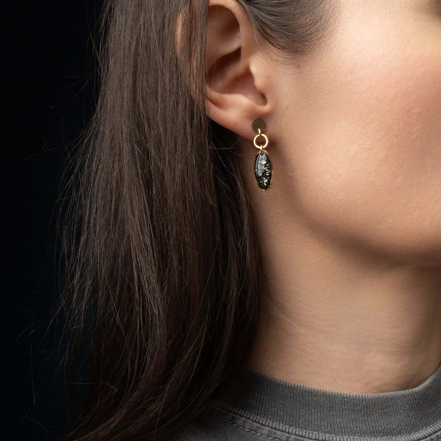 Close-up of a person wearing a gold earring with a dark gemstone on a black background