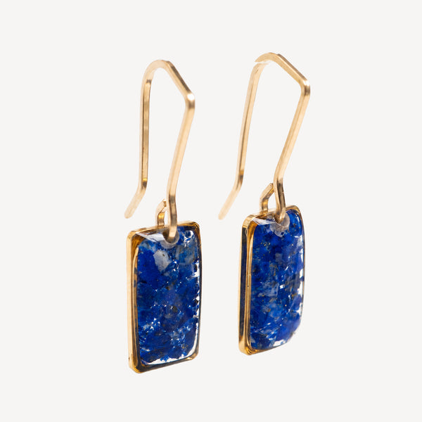 A pair of gold-tone dangle earrings with rectangular blue druzy stone pendants, shown against a plain off-white background.