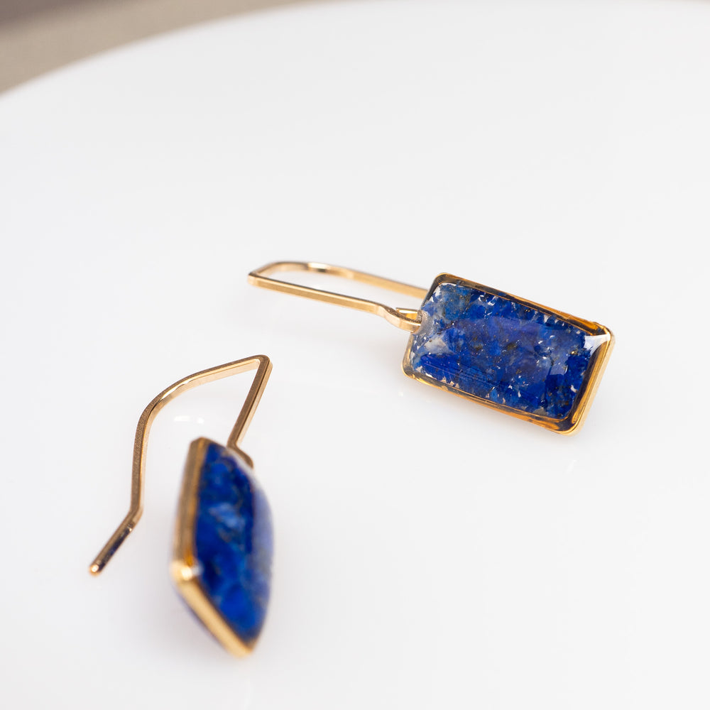 A pair of gold-tone dangle earrings with rectangular blue druzy stone pendants, shown against a plain off-white background.