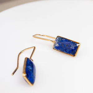 A pair of gold-tone drop earrings with rectangular and marquise-cut deep blue lapis lazuli stones, displayed on a clean white surface.