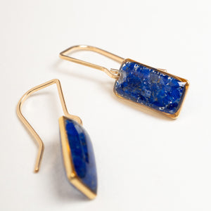 A pair of gold-tone drop earrings with rectangular and teardrop-shaped deep blue lapis lazuli stones, shown on a clean white background.