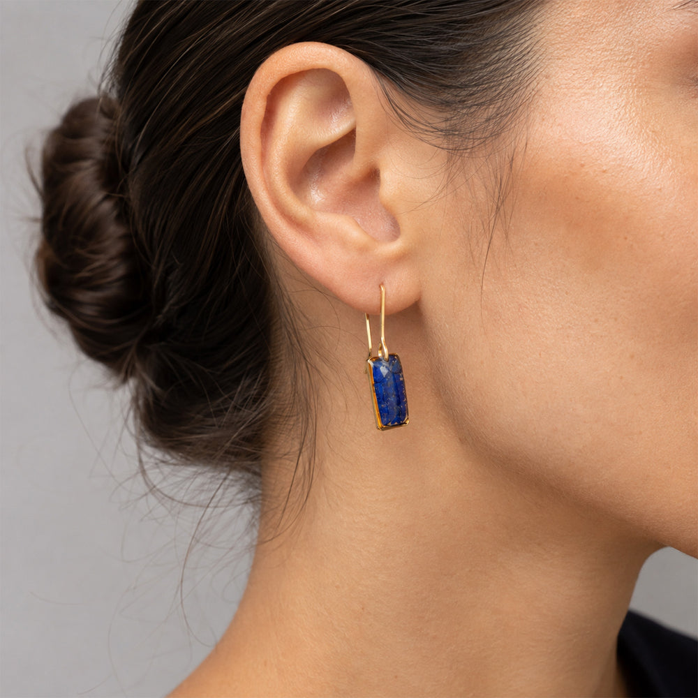A pair of gold-tone dangle earrings with rectangular blue druzy stone pendants, shown against a plain off-white background.