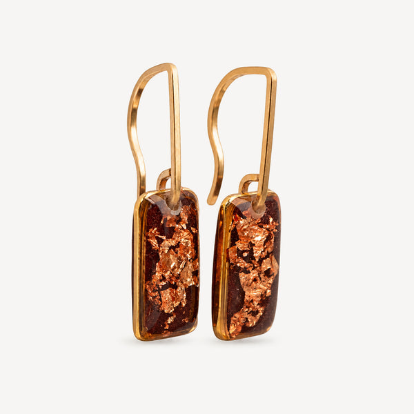 A pair of gold drop earrings featuring rectangular amber resin pendants with embedded copper-colored metallic flecks, set against a clean off-white background.