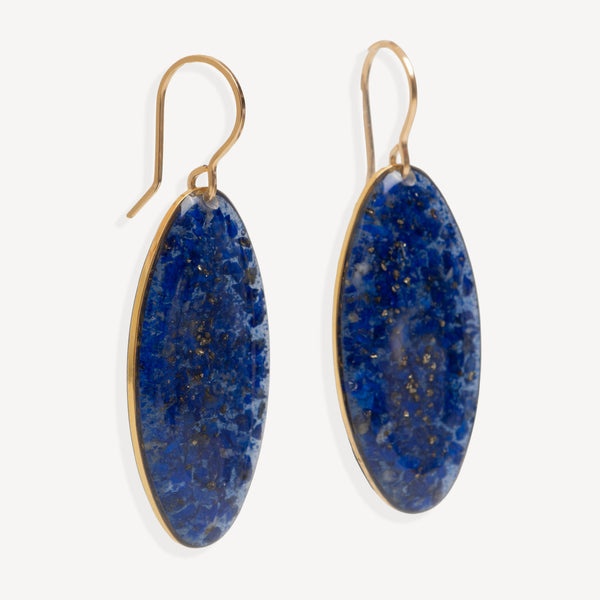A pair of gold drop earrings with oval blue lapis lazuli-style stones, shown against a light off-white background.