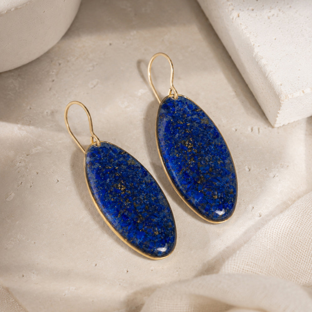 A pair of gold-tone drop earrings with oval blue agate pendants, shown against a plain off-white background.
