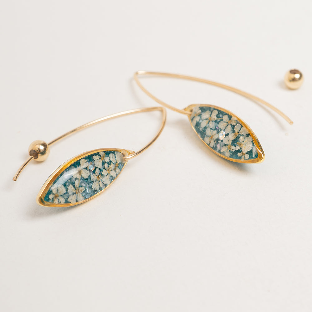 A pair of gold-tone dangle earrings with marquise-shaped turquoise and white floral resin inlays, shown against a light gray background.