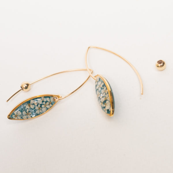 Gold-tone dangle earrings with marquise-shaped teal and white floral resin pendants, shown on a clean white background with one earring displayed flat and the other hanging to show the hook.