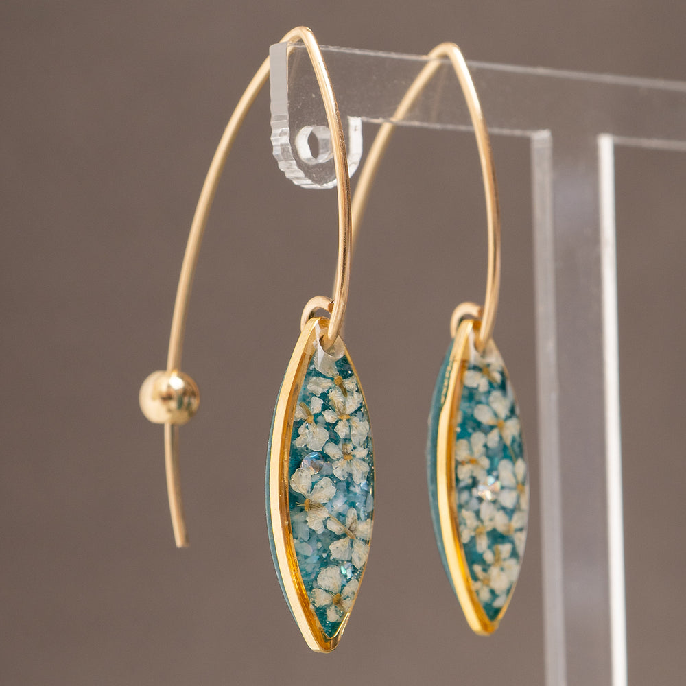 A pair of gold-tone dangle earrings with marquise-shaped turquoise and white floral resin inlays, shown against a light gray background.