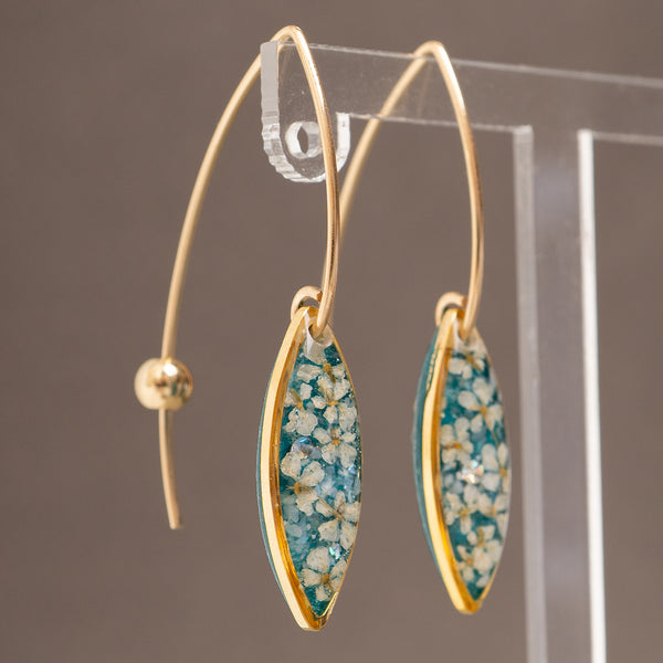 Gold hoop earrings with marquise-shaped dangles featuring a teal and white floral pattern, displayed on a clear acrylic stand against a neutral gray background.