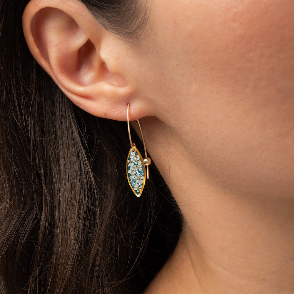 A pair of gold-tone dangle earrings with marquise-shaped turquoise and white floral resin inlays, shown against a light gray background.