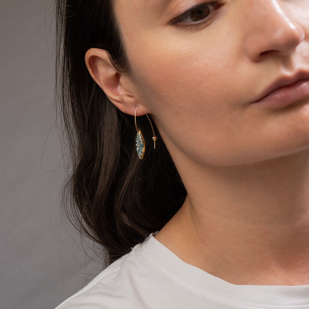 A pair of gold-tone dangle earrings with marquise-shaped turquoise and white floral resin inlays, shown against a light gray background.