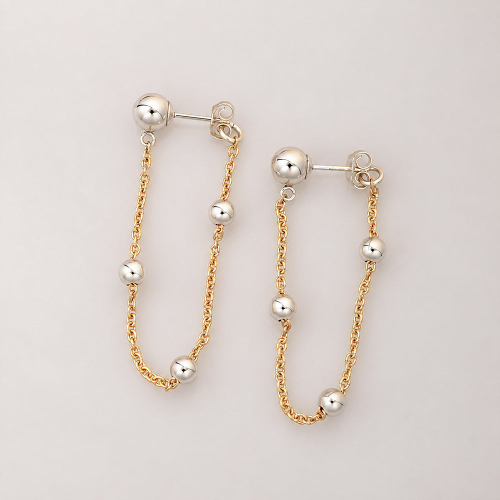 A pair of gold and silver drop earrings with spherical beads and delicate chains, displayed on a clean off-white background.