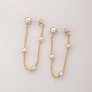 A pair of gold and silver drop earrings with small spherical beads on a light gray background.